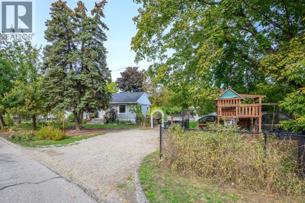 Gravel driveway leading to a light blue siding house with a children's playset on the right. - 2003 30 Avenue, Vernon