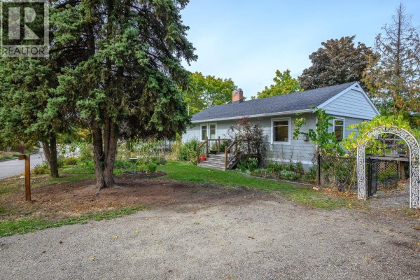Side view of a light blue siding house with a gravel driveway and mature trees. - 2003 30 Avenue, Vernon