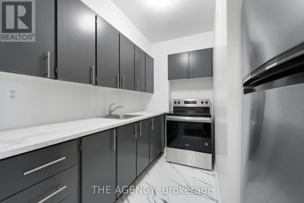 Kitchen with dark grey cabinets, white countertop, stainless steel appliances, and marble-patterned flooring. - 2004a - 2350 Dundas Street W, Toronto