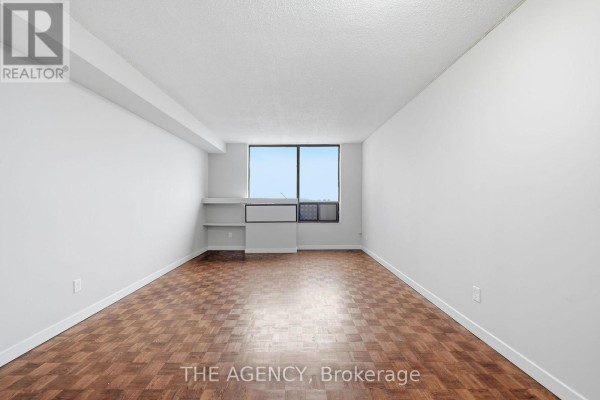 Spacious living area with parquet floors, white walls, built-in shelves, and a large window. - 2004a - 2350 Dundas Street W, Toronto