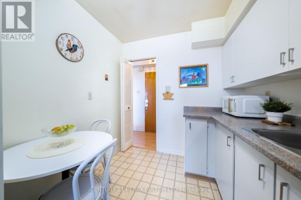 Small kitchen with white cabinets, granite countertops, a round table with four chairs, and a doorway. - 2006 - 1350 York Mills Road, Toronto