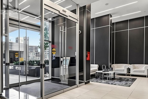 Lobby of modern apartment building with glass entrance, black wall paneling, and white seating area. - 2008 - 9 Bogert Avenue, Toronto