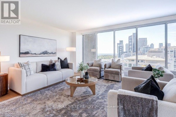 Living room with white sofas, a coffee table, and large windows overlooking a cityscape. - 2009 - 2045 Lake Shore Boulevard W, Toronto