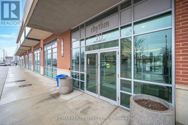 Entrance to the condo building with glass doors, brick accents, and planters. - 2009 - 215 Queen Street E, Brampton