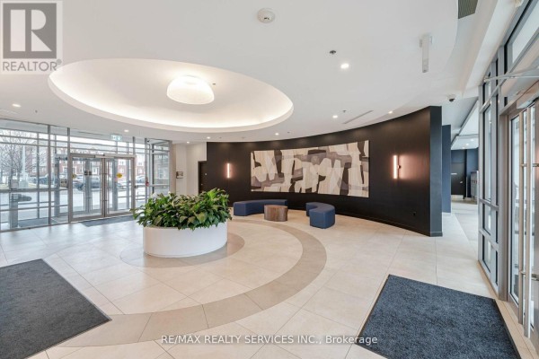 Modern lobby with beige tile floor, circular seating area, plants, and abstract art. - 2009 - 215 Queen Street E, Brampton