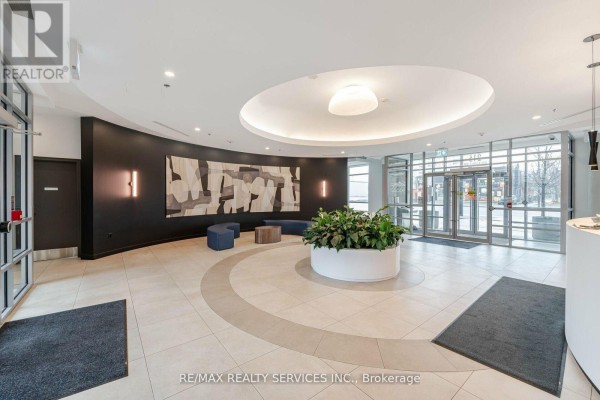 View of the condo lobby featuring curved dark wall, modern lighting, and glass entrance. - 2009 - 215 Queen Street E, Brampton