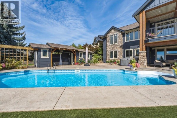 Backyard view of a house with a swimming pool, hot tub, and detached covered structure. - 2009 Apex Court, Vernon