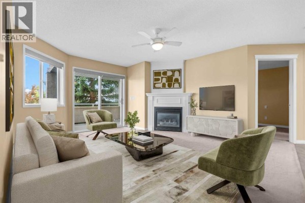 Living room with beige carpet, white fireplace, and glass sliding doors to balcony. - 201, 20 Country Hills View Nw, Calgary