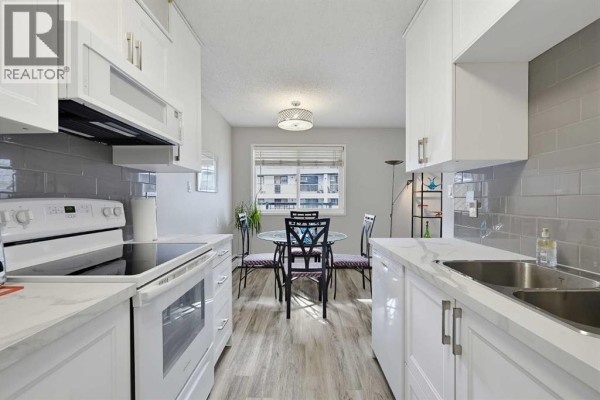 Kitchen view looking towards a dining area with a glass table and chairs. - 201, 617 56 Avenue Sw, Calgary