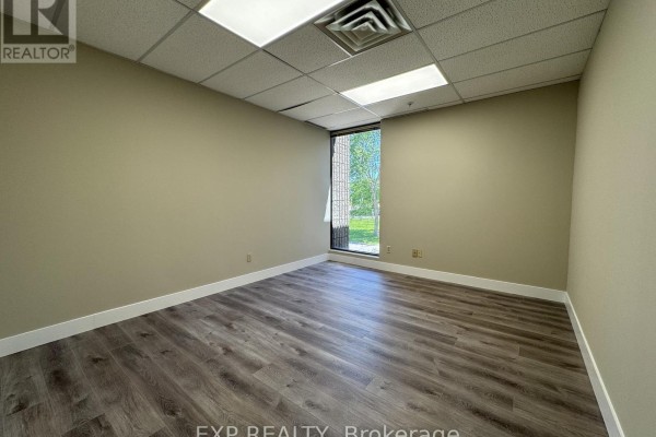 Empty room with beige walls, wood-look flooring, and a large window overlooking trees. - 201 - 101 Cherryhill Boulevard, London North