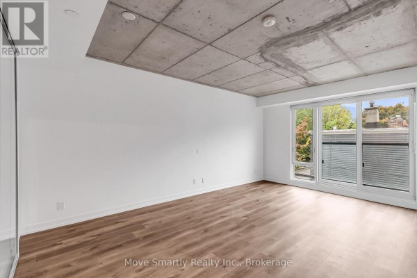 Empty room with hardwood floors, concrete ceiling, and a sliding glass door leading to a balcony. - 201 - 115 Larchmount Avenue, Toronto
