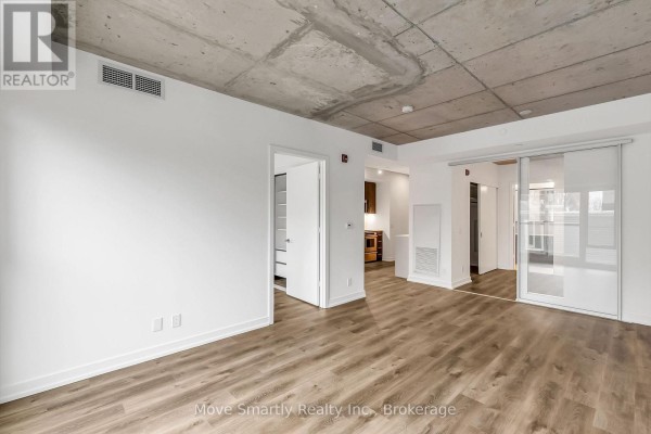 Living space with hardwood floors, white walls, concrete ceiling, and doorways to other rooms. - 201 - 115 Larchmount Avenue, Toronto