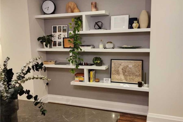 Close-up of white staggered shelves mounted on a grey wall, decorated with books, plants, and art. - 201 - 15 Ennerdale Road, Toronto
