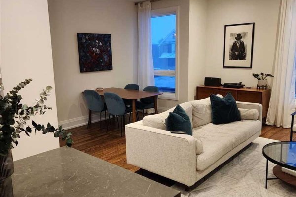 Living and dining area with a cream sofa, wood dining table with blue chairs, and artwork. - 201 - 15 Ennerdale Road, Toronto
