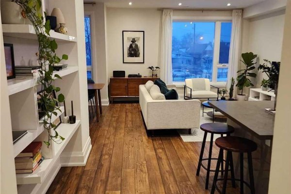 Wide view of the living and dining area showing a sofa, dining set, shelving, and a large window. - 201 - 15 Ennerdale Road, Toronto