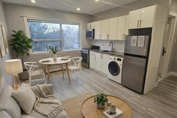 Living area and kitchen with gray walls, white cabinets, stainless steel appliances, and a small dining table. - 201 - 1566 Avenue Road, Toronto