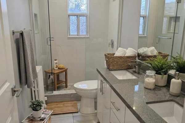 A modern bathroom with a double vanity, gray countertops, a glass-enclosed shower, and white tiled walls. - 201 - 1566 Avenue Road, Toronto