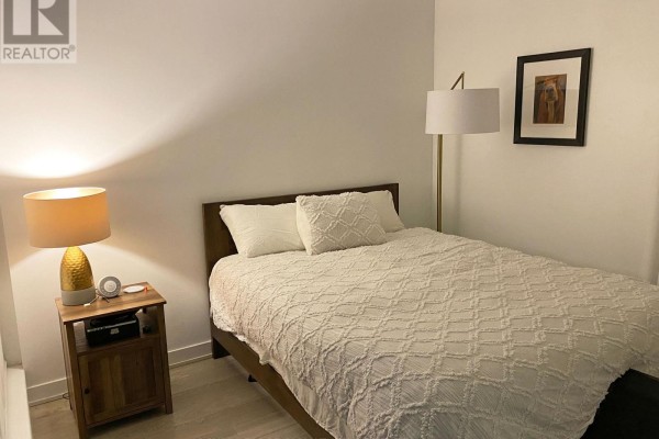 Bedroom with a queen-sized bed, nightstand, and a floor lamp. - 201 - 185 Roehampton Avenue, Toronto