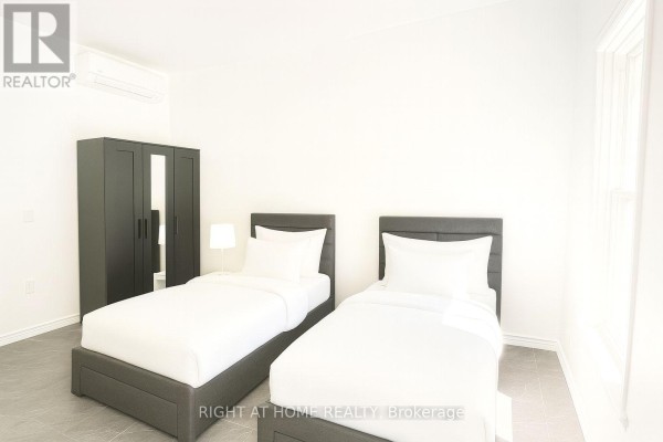Two beds with white linens, a dark wardrobe, and an air conditioning unit in a white room. - 201 - 198-200 Queen Street W, Toronto
