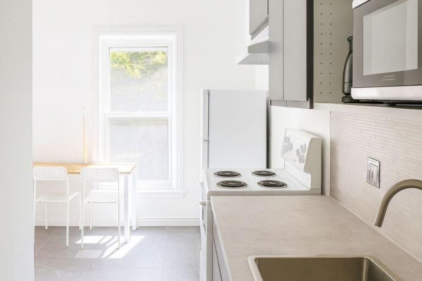 A small kitchen area with a white stove, sink, microwave, and a small table and chairs. - 201 - 198-200 Queen Street W, Toronto