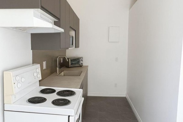 A compact kitchen with a white stove, gray cabinets, sink, and microwave against a white wall. - 201 - 198-200 Queen Street W, Toronto