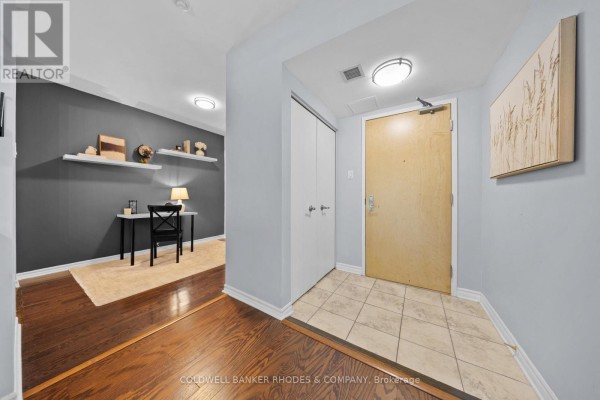 Apartment entryway with tiled floor, light blue walls, and wood-paneled door. - 201 - 200 Lett Street, Ottawa