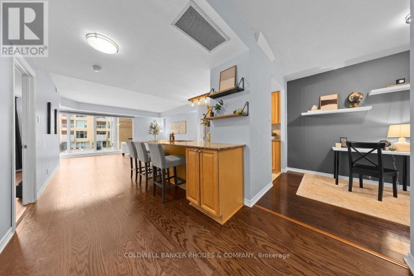 Open-concept living area with a breakfast bar, granite countertop, and wooden floors. - 201 - 200 Lett Street, Ottawa
