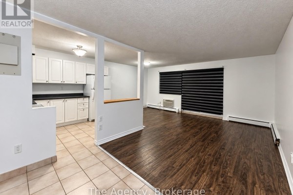 Open concept living area and kitchen with white cabinets, dark wood floors, and sliding glass doors. - 201 - 242 Oakdale Avenue, St  Catharines