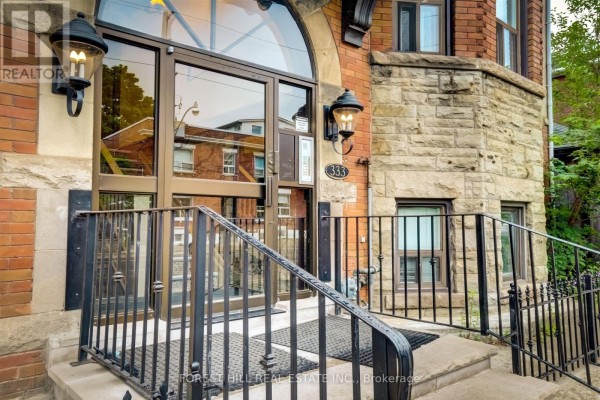 Close-up of building entrance with glass doors, lanterns, and stone surround. - 201 - 333 Harbord Street, Toronto