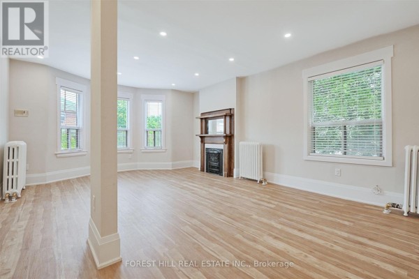 Living room with light wood floors, white walls, fireplace, and radiators. - 201 - 333 Harbord Street, Toronto