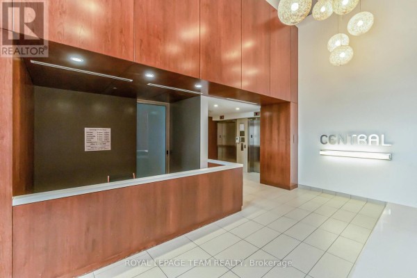 Building lobby with a reception desk, wood paneling, elevators, and tiled floor. - 201 - 354 Gladstone Avenue, Ottawa