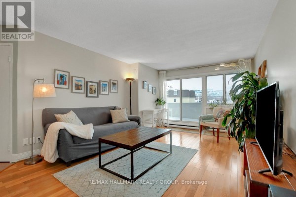 Living room with a grey sofa, wooden coffee table, hardwood floors, and a large sliding glass door. - 201 - 40 Landry Street, Ottawa