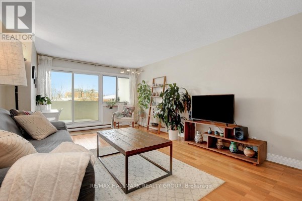 Living room with a sofa, coffee table, television, hardwood floors, and a view of a balcony. - 201 - 40 Landry Street, Ottawa