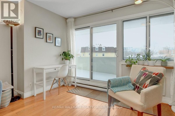 Corner of a living room with a white desk, chair, armchair, and sliding glass doors. - 201 - 40 Landry Street, Ottawa