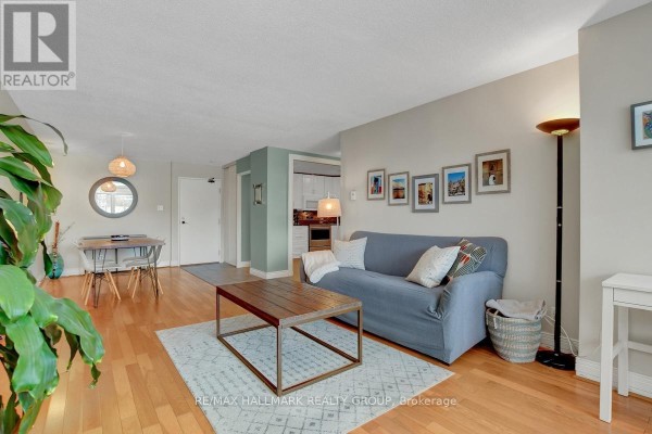 Living room and dining area with wood floors, sofa, dining table, and doorway to kitchen. - 201 - 40 Landry Street, Ottawa