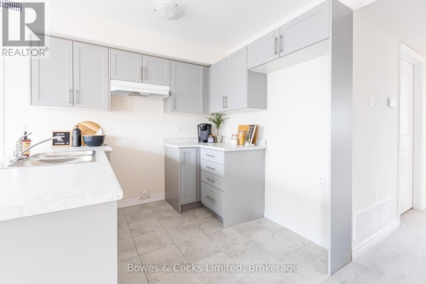 Kitchen with grey cabinets, island, and dining area with two windows. - 201 - 48 Maple Avenue, Asphodel Norwood