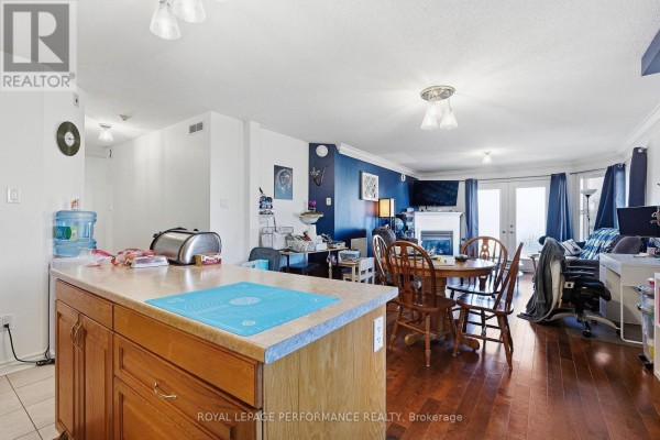 View of the living and dining area from the kitchen, showing a fireplace, seating, and wooden dining set. - 201 - 770 Principale Street, Casselman