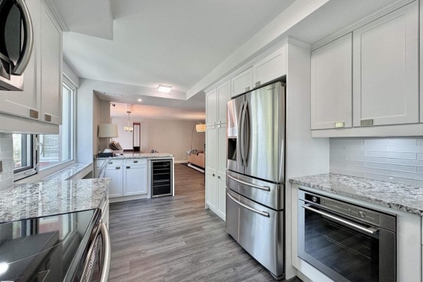 Modern white kitchen with granite countertops, stainless steel appliances, and a wine fridge. - #201 10010 119 St Nw, Edmonton
