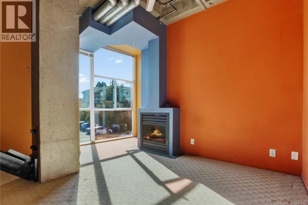 Living area with a modern gas fireplace, concrete pillar, and orange and blue accent walls. - 201 1061 Fort St, Victoria
