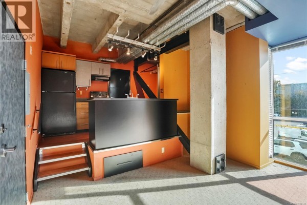Living room with large windows, a lit gas fireplace, and colorful walls in yellow, blue, and orange. - 201 1061 Fort St, Victoria