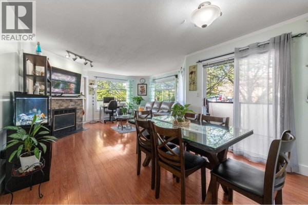 Living and dining area with fireplace, sofa, dining table, and sliding glass doors. - 201 175 W 4th Street, North Vancouver