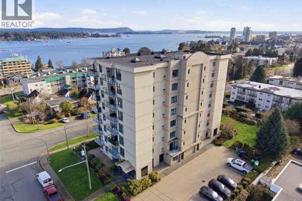 Outdoor balcony with patio furniture, glass railing, and a distant water view. - 201 225 Rosehill St, Nanaimo