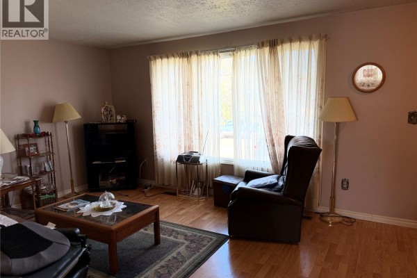 Living room with pink walls, patterned curtains over large windows, and wood floors. - 201 2nd Avenue, Melfort