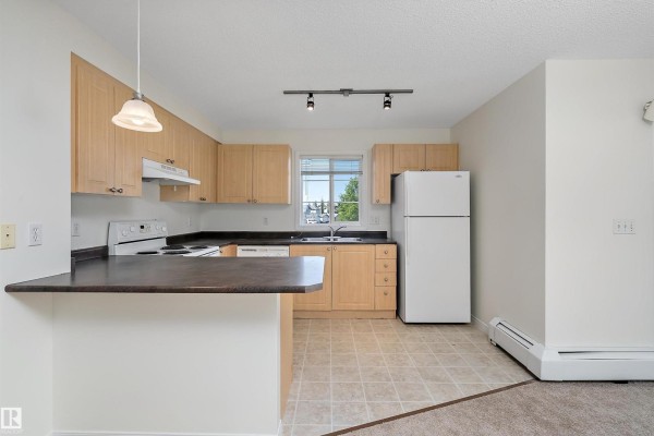 Kitchen with light wood cabinets, black countertops, white appliances, and a breakfast bar. - #201 630 Mcallister Lo Sw, Edmonton