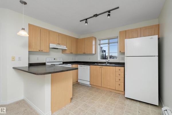 Kitchen with light wood cabinets, black countertops, white appliances, and a breakfast bar. - #201 630 Mcallister Lo Sw, Edmonton