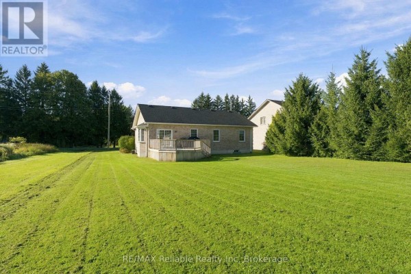 Rear view of a brick bungalow with a wooden deck and surrounding trees. - 201 Cowper Street, Central Huron