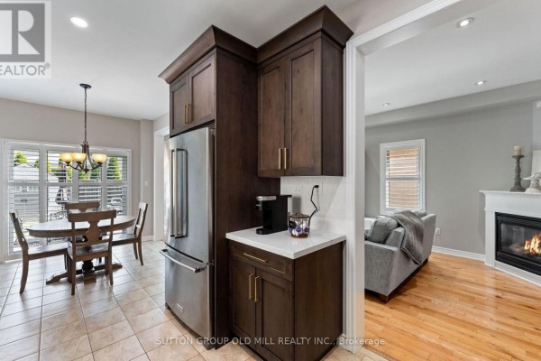 Kitchen area with stainless steel refrigerator, dark wood cabinetry, and a glimpse into a living room with a fireplace. - 201 Vellore Park Avenue, Vaughan