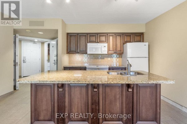 Kitchen island with granite countertop and dark wood cabinets, opening to a hallway. - 2010/2011 - 90 Highland Drive, Oro Medonte