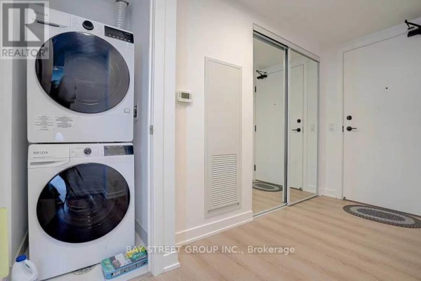 Stacked white washer and dryer next to a closet with mirrored sliding doors. - 2011 - 100 Queen Street E, Toronto