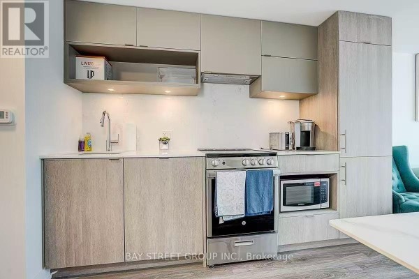 Compact kitchen with stainless steel appliances, light wood lower cabinets, and grey uppers. - 2011 - 100 Queen Street E, Toronto